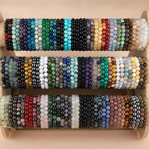 May include: A display of colorful beaded bracelets made with various semi-precious stones. The bracelets are arranged in rows on a wooden stand.