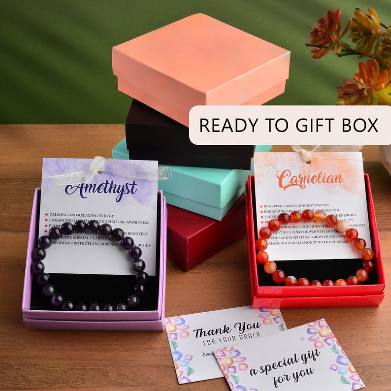 May include: Two gift boxes with gemstone bracelets, one amethyst and one carnelian, with descriptions of their properties. The boxes are stacked on top of each other and are ready to be gifted. The boxes are surrounded by a thank you card and a card that says "a special gift for you".