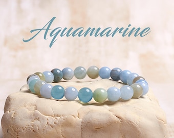 May include: Aquamarine gemstone bracelet with light blue, green, and white beads. The bracelet is on a light brown surface.