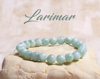 May include: A light blue Larimar gemstone bracelet with round beads. The bracelet is on a light beige surface.