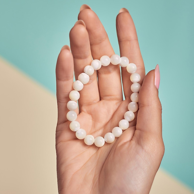 May include: A white pearl bracelet with a simple design. The bracelet is made of round, smooth pearls that are strung together on a clear elastic cord.