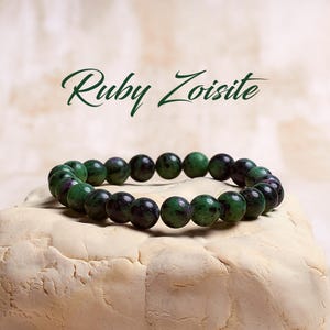 May include: A green and black ruby zoisite gemstone bracelet. The bracelet is made of round beads and is strung on elastic.