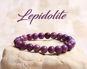 May include: A purple Lepidolite gemstone bracelet with round beads. The bracelet is on a white rock.