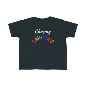 Puede incluir: Una camiseta azul oscuro con el texto "Chasing Rainbows" en blanco con un arcoíris sobre la palabra "Rainbows".