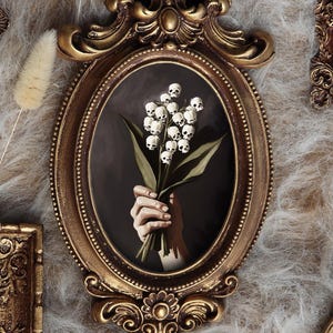 May include: An assortment of antique-style framed art pieces. Each frame is a different shape and size, with ornate gold and bronze finishes. The artwork within each frame depicts a hand holding a bouquet of white flowers against a dark background.