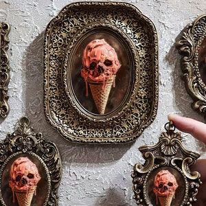 Peut inclure: Cinq cadres de style antique, dorés, chacun présentant une image d'une glace fondante en forme de crâne. La glace est d'une couleur rouge-orangé, créant un contraste saisissant avec les cadres.