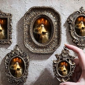 以下が含まれることがあります： 様々な形の装飾的なアンティーク風フレーム。それぞれに本を読む幽霊の不気味な画像が収められています。フレームは濃い金色で、幽霊のイラストにはろうそくが描かれています。手で1つのフレームを持っています。