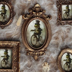 May include: A selection of antique-style framed artworks. Each frame, in gold and bronze tones, showcases a whimsical illustration of a frog on a bicycle. The frames are in various shapes, including oval, rectangular, and ornate designs.