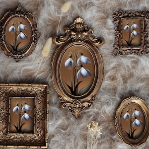 May include: An assortment of antique gold-framed art pieces, each featuring a painting of white and blue snowdrop flowers against a brown background. The frames vary in shape, including oval, rectangular, and ornate designs. The arrangement is set on a textured, light-colored surface.