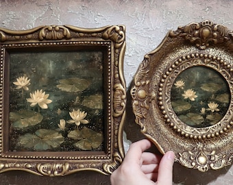 May include: Two ornate gold picture frames with a painting of white water lilies in a pond. The frames have intricate details and a beaded border.