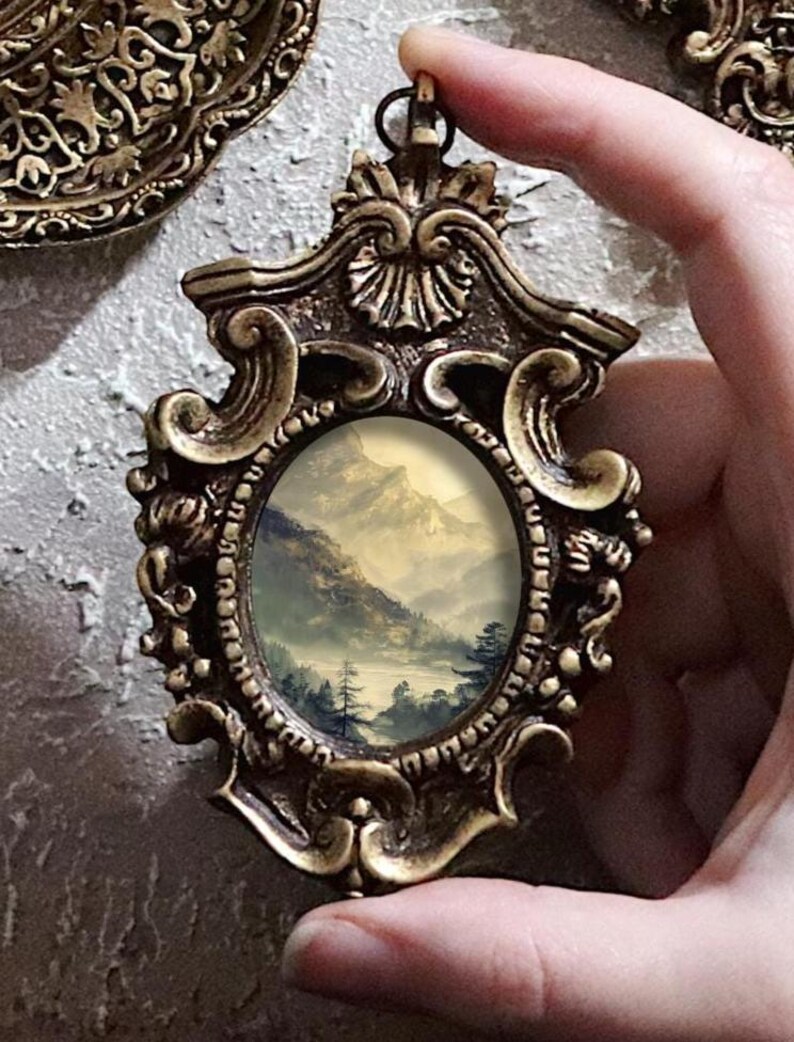 K&ouml;nnte beinhalten: Verziertes Anh&auml;nger im antiken Stil mit einer Miniatur-Landschaftsmalerei. Der Anh&auml;nger hat einen detaillierten, goldfarbenen Rahmen mit Schn&ouml;rkeln und eine kleine Schlaufe zum Aufh&auml;ngen. Das Gem&auml;lde zeigt eine neblige Berglandschaft mit B&auml;umen und einem See.