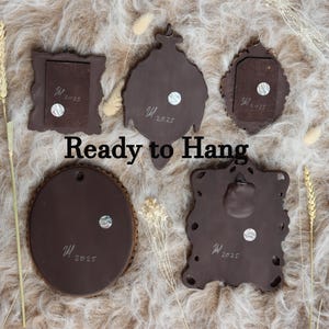 May include: Five brown decorative wall hangings of various shapes, including a square, oval, and ornate designs. Each piece has a textured surface and a small, round magnet. The text "Ready to Hang" is displayed in the image.