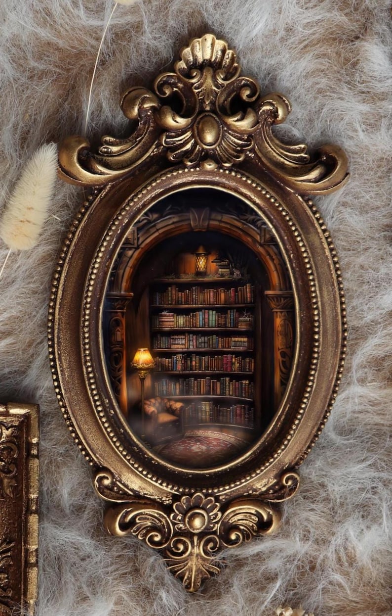 May include: Ornate gold-colored oval frame with a detailed interior scene of a cozy library. The library features bookshelves filled with books, a warm lamp, and a small seating area. The frame is set against a textured, neutral background.