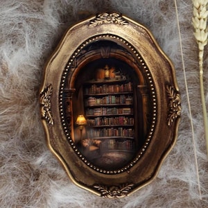 May include: An oval, antique-style frame with a miniature library scene inside. The frame is gold-colored with ornate detailing. The miniature scene features a bookshelf filled with books, a lamp, and a cozy reading nook.