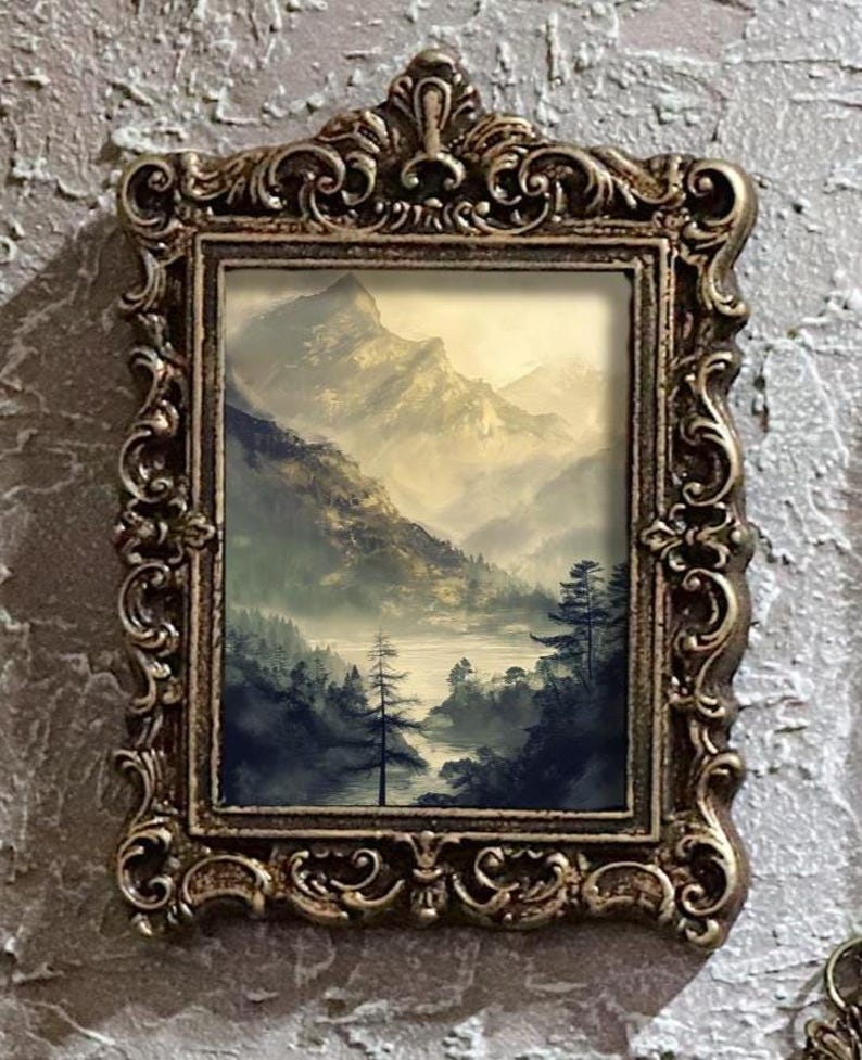 K&ouml;nnte beinhalten: Ein gerahmtes Landschaftsgem&auml;lde mit einer Bergkette, einem Fluss und B&auml;umen. Das Gem&auml;lde befindet sich in einem dekorativen, goldfarbenen Rahmen mit aufwendigen Details. Das Kunstwerk hat eine ged&auml;mpfte Farbpalette mit Gr&uuml;n-, Braun- und Graut&ouml;nen.
