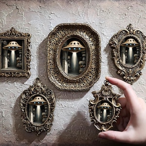 May include: Ornate, antique-style frames in various shapes, each featuring a miniature scene of a UFO emitting a beam of light. The frames are gold-toned and detailed, creating a vintage aesthetic. A hand holds one of the frames.