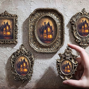 May include: Five ornate gold picture frames with a dark, mysterious house with lit windows in each. The frames are arranged on a textured wall.