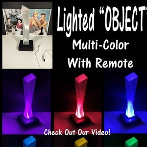 Può includere: Una scultura in acrilico trasparente con una luce all'interno. La scultura è illuminata da una luce LED multicolore e viene fornita con un telecomando. La scultura è mostrata in sei colori diversi: viola, rosso, blu, azzurro, giallo e verde. Il testo "Lighted "OBJECT" Multi-Color With Remote" è mostrato nella parte superiore dell'immagine. Il testo "Check Out Our Video!" è mostrato nella parte inferiore dell'immagine.