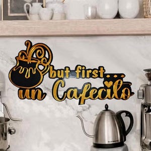 May include: A kitchen counter with a silver stand mixer, a stainless steel kettle, and an espresso machine. A decorative sign with the text "but first un Cafecito" is mounted on the wall. The scene suggests a coffee station.