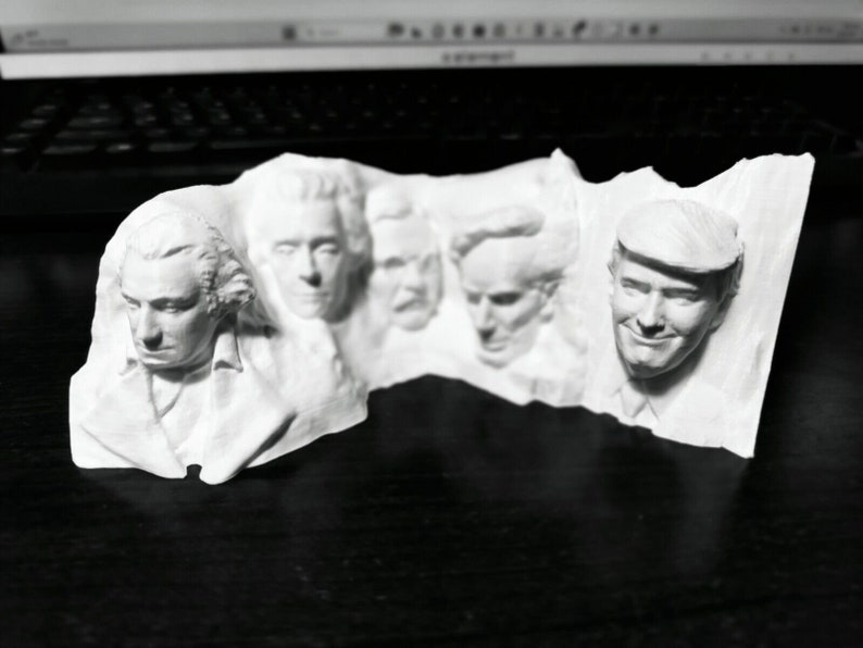 Op de afbeelding: Een witte 3D-geprinte sculptuur met de gezichten van verschillende Amerikaanse presidenten. De sculptuur heeft gedetailleerde gelaatstrekken en is waarschijnlijk een decoratief item of een uniek kunstwerk. De presidenten zijn in een rij gerangschikt, waarbij elk gezicht duidelijk zichtbaar is.