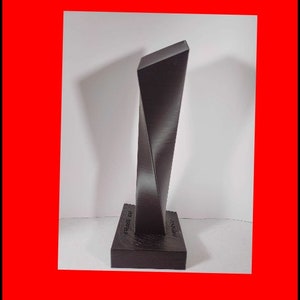 May include: A black, twisted, abstract sculpture on a black base. The base has the words "DESIGN" and "MADE IN ITALY" printed on it.