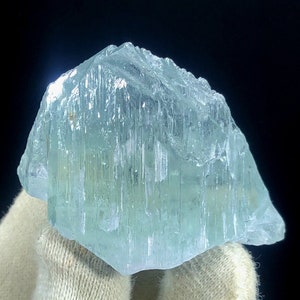 May include: A large, light blue aquamarine crystal with a smooth, polished surface. The crystal has a slightly cloudy appearance and is shaped like a pyramid.