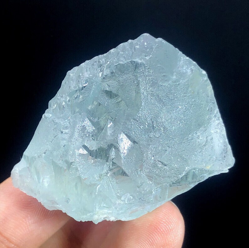 May include: A large, light blue aquamarine crystal with a rough, natural surface. The crystal has a translucent appearance and shows internal facets.