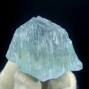 May include: A large, light blue aquamarine crystal with striations and a translucent appearance.