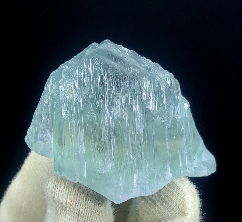 May include: A large, light blue aquamarine crystal with striations and a translucent appearance.