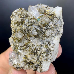 May include: A close-up of a mineral specimen featuring a matrix of white quartz with embedded, needle-like crystals in shades of green and black. Several clear quartz crystals are also visible, along with a small, turquoise-colored mineral inclusion.
