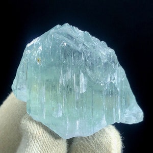 May include: A large, light blue aquamarine crystal with a striated surface. The crystal is translucent and has a slight green hue.