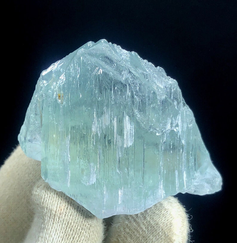 May include: A large, light blue aquamarine crystal with a striated surface. The crystal is translucent and has a slight green hue.