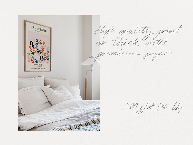 May include: A white bedroom with a framed print on the wall. The print features a pink background with the word "FEMINISME" and a design of colorful gender symbols. The text "LA REVOLUTION" is also included on the print. The bed has white linens and pillows. A lamp is on a wooden stand next to the bed. The text "High quality print on thick matte premium paper 200 g/m&sup2; (80 lb)" is written in cursive on a white background.