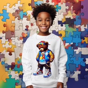 May include: White sweatshirt with a colorful cartoon bear wearing a blue and yellow jacket, a blue and white hat, and blue and white sneakers. The bear is holding a gold chain in one hand and has a gold chain around its neck. The bear is standing on a white background.