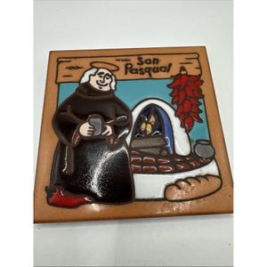 May include: Square ceramic tile featuring a depiction of San Pasqual, a friar, with a halo, holding a vessel. The tile includes a sign that reads "San Pasqual", a red chili pepper, and a traditional oven. The tile has a brown border.