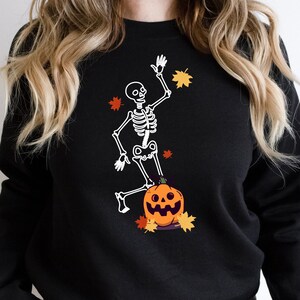 May include: Black sweatshirt with a white skeleton dancing on top of a jack-o'-lantern. The skeleton is wearing a pumpkin hat and holding a leaf.