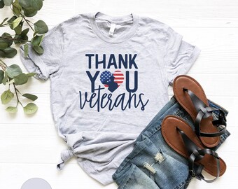 May include: A gray t-shirt with the text "THANK YOU veterans" in navy blue. The "O" in "YOU" is replaced with a red, white, and blue heart with a silhouette of a person inside.