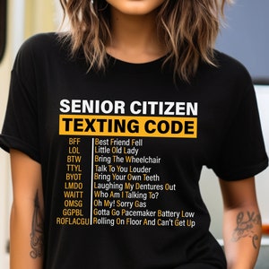May include: Black t-shirt with a white graphic that says "Senior Citizen Texting Code" and lists common texting abbreviations and their meanings.