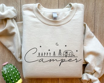 Könnte beinhalten: Ein cremefarbener Pullover mit dem Schriftzug "HAPPY Camper" in schwarzer Schrift. Ein kleiner schwarzer Wohnwagen mit einem Herzen an der Seite ist neben einem Halbmond und Sternen abgebildet.