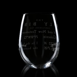 May include: A clear glass wine glass with the text "CONTAINING THE HOLY BIBLE" and "Genesis" and "Old and New Testament" etched on the side.