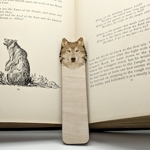 Puede incluir: Un marcapáginas de madera con un diseño de cabeza de lobo. El marcapáginas es de color marrón claro y tiene una veta de madera natural. La cabeza de lobo está en el centro del marcapáginas y mira hacia adelante. El marcapáginas mide aproximadamente 25 cm de largo y 5 cm de ancho.
