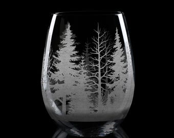 May include: A clear glass wine glass with an etched design of a winter forest scene. The design features white trees against a clear background.