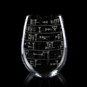 May include: A clear glass wine glass with a pattern of ancient cuneiform script etched into the surface.