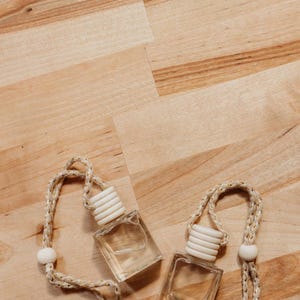 May include: Two clear glass bottles with white lids and gold string hanging from them. The bottles are on a light brown wooden surface.