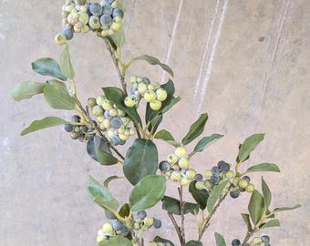 May include: A faux floral stem featuring clusters of small, round berries in shades of blue and green. The berries are interspersed among green leaves. The stem is brown and has a natural appearance, suitable for home decor or crafting projects.