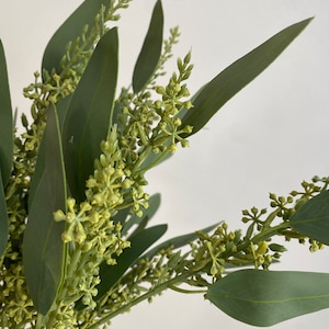 May include: A bunch of artificial eucalyptus sprigs with green leaves and small yellow flower buds.