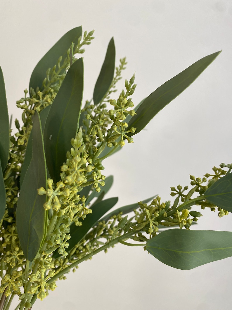 May include: A bunch of artificial eucalyptus sprigs with green leaves and small yellow flower buds.