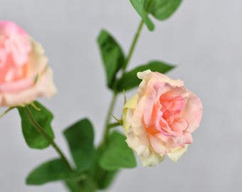 May include: Two artificial pink and cream roses with green stems and leaves.