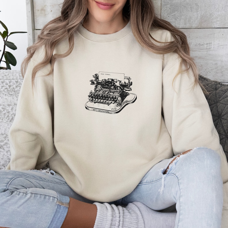 May include: A beige sweatshirt with a black and white illustration of a vintage typewriter with the text "Dear Friend." printed on the paper.