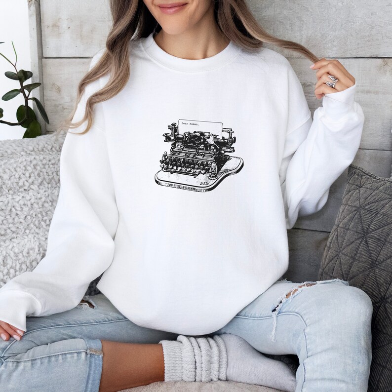 May include: White sweatshirt with a black and white illustration of a vintage typewriter. The typewriter has a paper carriage that says "Dear Editor."